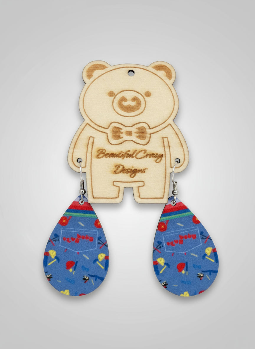 Wooden bear-shaped pendant with Good Guy doll suspenders, colorful teardrop earrings on a gray background