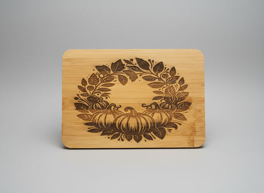 Wooden cutting board with pumpkin and leaf design on a gray background