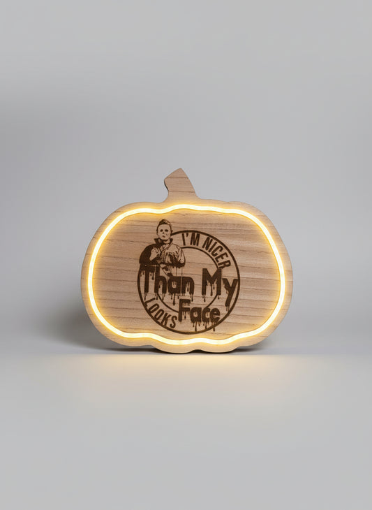 Wooden pumpkin-shaped novelty sign with engraved text and lighting effect on a dark background