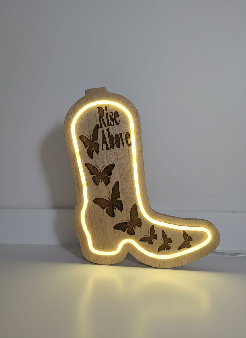 Wooden boot-shaped sign with 'Rise Above' and butterfly designs, illuminated from within.