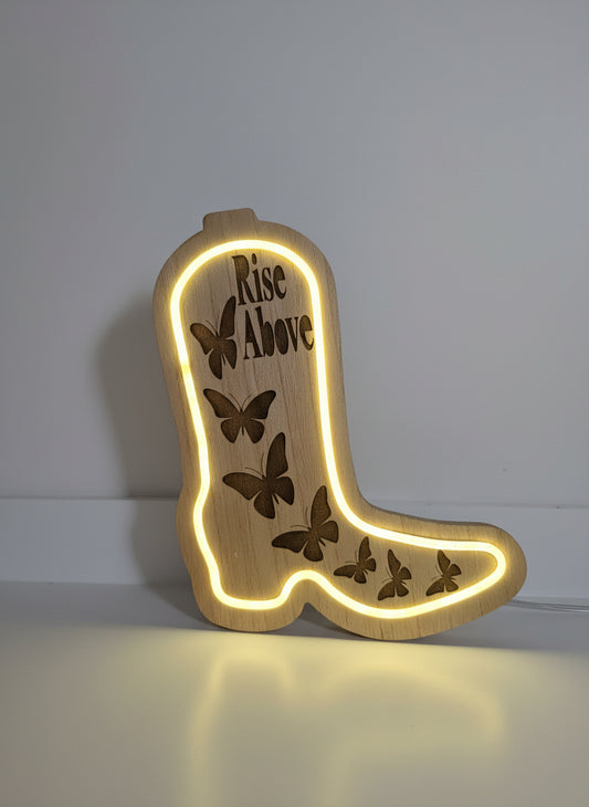 Wooden boot-shaped sign with 'Rise Above' and butterfly designs, illuminated from within.