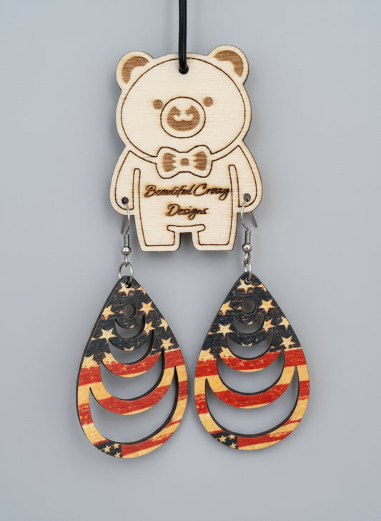 Wooden earrings with American flag design on a wooden background with 'Beautiful Creepy Designs' tag.